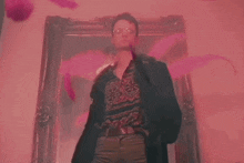a man is standing in front of a painting with pink feathers coming out of it .