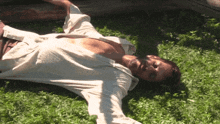 a man in a white shirt is laying on the grass with his arms outstretched