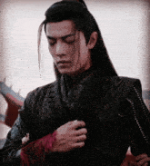 a man with long hair is wearing a black jacket and a red shirt