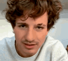 a close up of a man with curly hair wearing a white shirt and a necklace .