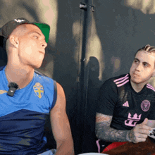 two men sitting at a table with one wearing a shirt that says fc on it