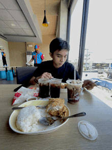 a boy sits at a table with a jollibee cup