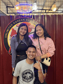 three people are posing for a picture in front of a sign that says unlimited korean bbq and locos norte