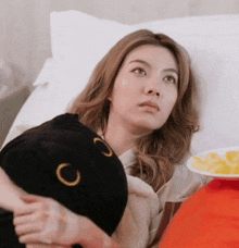 a woman laying in a bed holding a black cat pillow