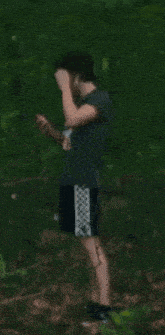 a young man in a gray shirt and black shorts stands in the woods