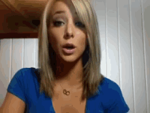 a blonde woman wearing a blue shirt and a necklace with the letter g on it