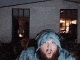 a man with a beard wearing headphones and a blue hoodie is looking at the camera