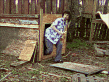 a man in a floral shirt is standing outside of a dog house