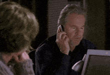 a man is blowing his nose while sitting at a desk in front of a laptop .