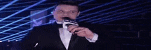 a man in a tuxedo is holding a microphone in his hand and talking into it .