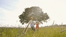 a boy and a girl are playing in a field with a tree in the background