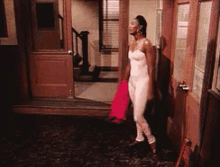 a woman in a white bodysuit is standing in front of a door holding a red blanket .