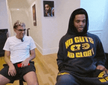 a man in a no guts no glory hoodie sits next to another man