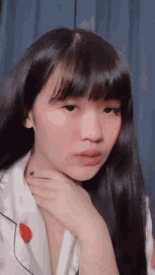a girl with long black hair and bangs looks at the camera with her hand on her neck