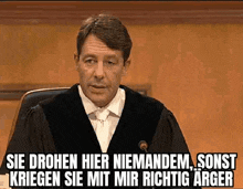 a man in a judge 's robe is sitting in front of a microphone with a caption in german .