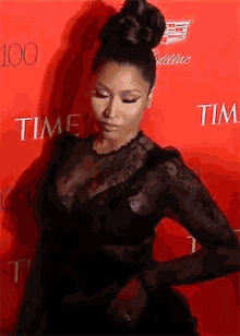 a woman in a black dress is standing in front of a red wall with the word time on it