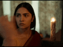 a woman in a red sari is standing in front of a candle .