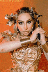 a woman in a gold costume is holding a sword and has a flower in her hair