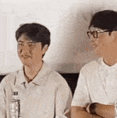 two men are sitting next to each other with their arms crossed and a bottle of water .