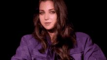 a woman in a purple jacket is smiling and holding her hair in her hands .