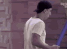 a man wearing a baseball cap and a white shirt is standing next to a wall .