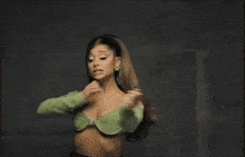 ariana grande is wearing a green top and earrings while dancing in front of a mirror .