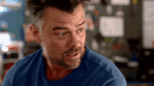 a man with a beard and a mohawk is wearing a blue shirt and looking at the camera .