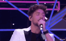 a man in a tuxedo is singing into a microphone .