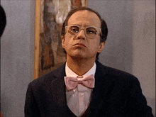 a man wearing glasses and a pink bow tie looks serious