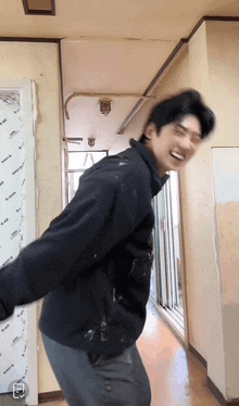 a man in a black jacket is dancing in a hallway with a white sheet on the wall that says ' west ' on it
