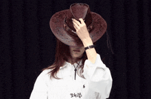 a woman wearing a cowboy hat covers her face