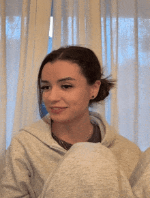 a woman sitting in front of a window with white curtains