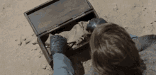 a person wearing leather gloves is looking into a wooden box on the ground .
