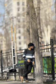 a man leans against a tree in a park while looking at his phone