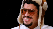 a man wearing a furry hat and sunglasses smiles