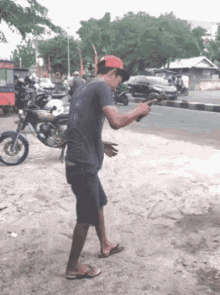 a man in a red hat is standing on the side of the road looking at his phone .