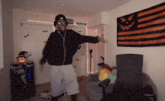 a man wearing headphones is dancing in a room with an orange and black flag hanging on the wall