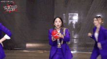 two women in purple suits are dancing in front of a sign that says " the bomb dance "