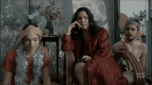 a woman in a red robe sits in a chair next to a man smoking a cigarette