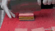 a person is cutting a piece of candy with a knife on a red cutting board made in animatica