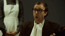 a man with glasses and a bow tie is sitting in front of a maid