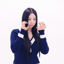 a woman with long black hair wearing a blue sweater with a white stripe on the sleeves