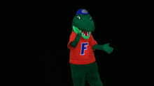 a green crocodile mascot wearing a red shirt with the letter f on it
