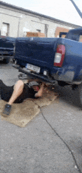 a man is laying on the ground under a blue truck with a license plate that says tpp 5237 .