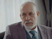 a man with a beard wearing a suit and tie looks at the camera