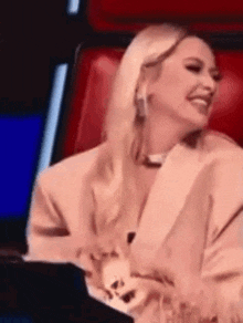 a woman in a suit is sitting in a red chair laughing .