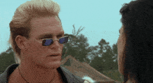 a man wearing sunglasses and a mullet talks to a woman