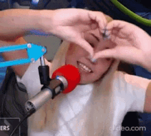 a woman is making a heart shape with her hands while standing in front of a microphone .