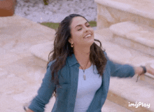 a woman in a blue shirt is smiling with her arms outstretched in front of a set of stairs