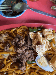 a plate of noodles with meat and vegetables with a spoon and fork on a table